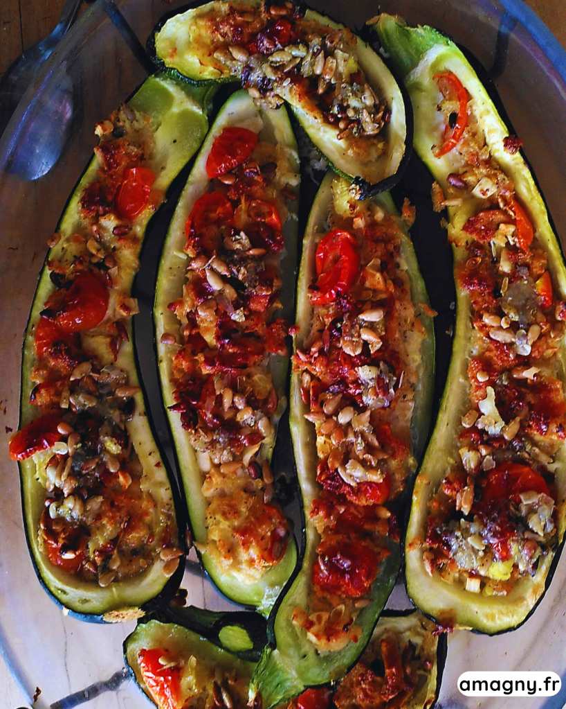 Plat de courgettes farcies façon Ottolenghi, garnies de légumes et servies avec une sauce vierge aux pignons.
