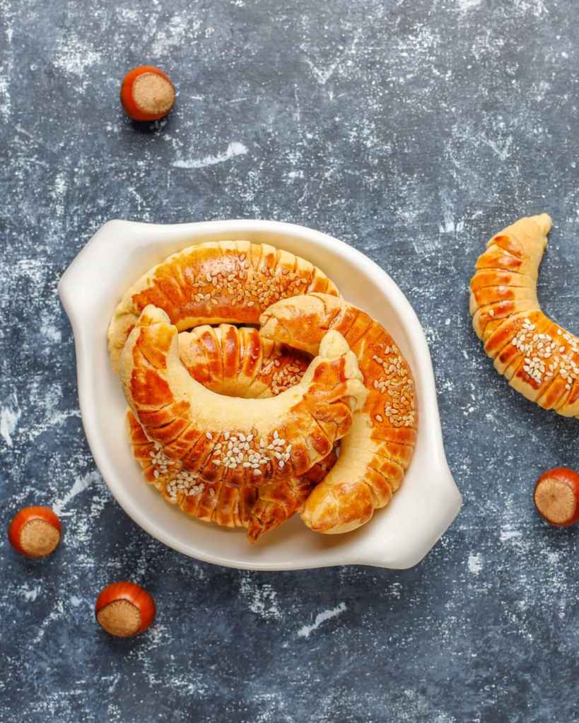 Croissants dorés aux noisettes, saupoudrés de graines de sésame sur assiette sombre.