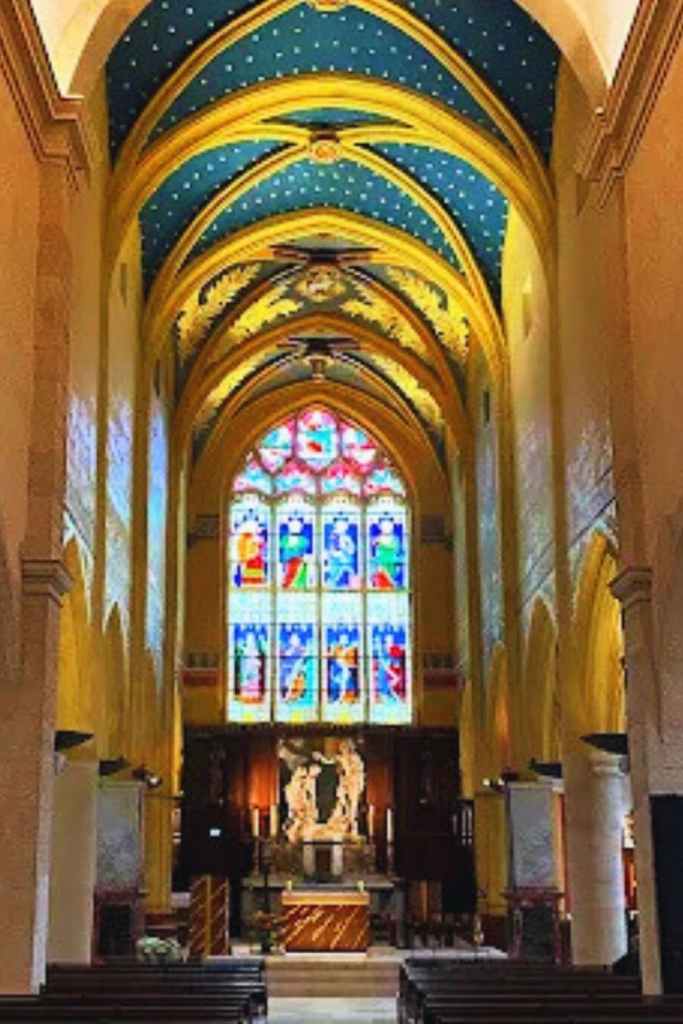 Intérieur d’église avec voûtes bleues étoilées, vitrail coloré et autel éclairé.