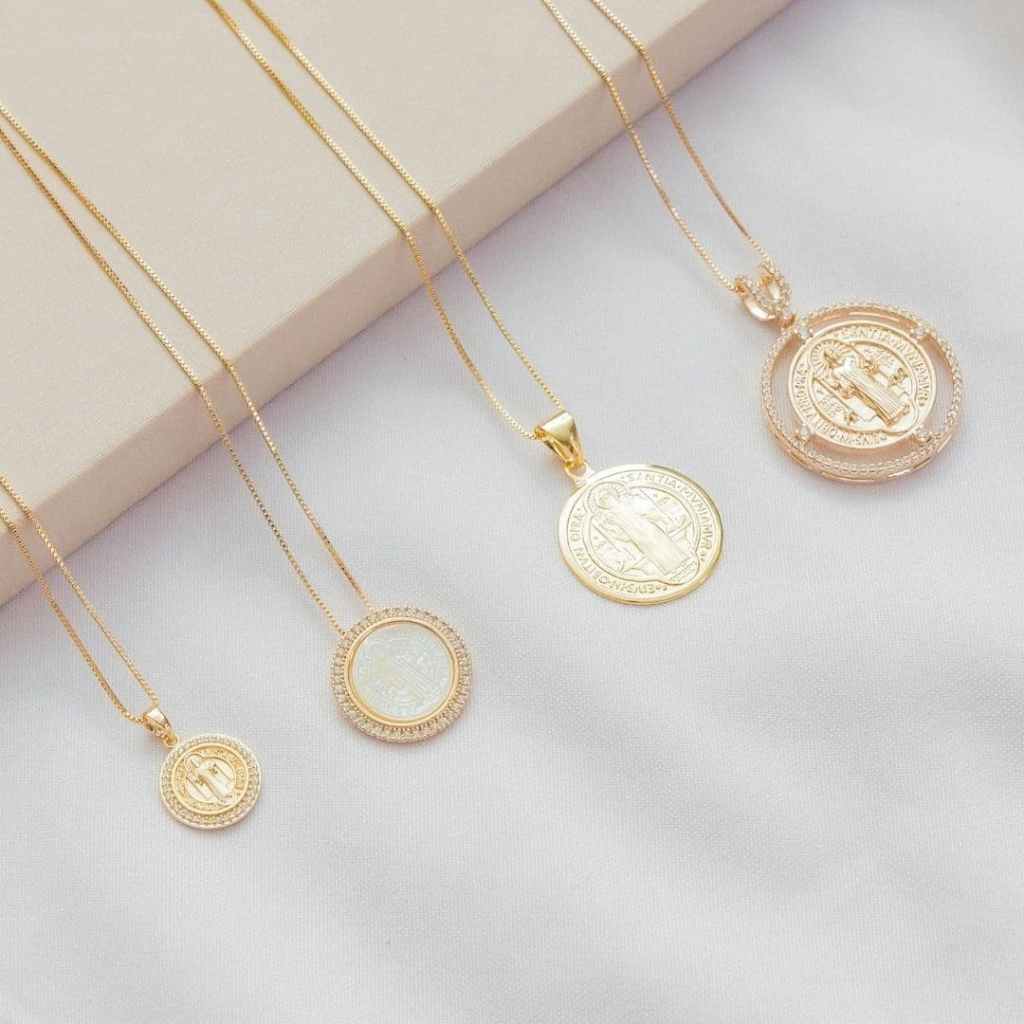 Quatre colliers dorés avec médailles religieuses posés sur un tissu clair.