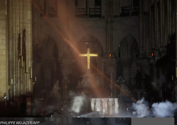 Intérieur de Notre-Dame de Paris enveloppé de fumée avec une croix dorée illuminée après l’incendie.