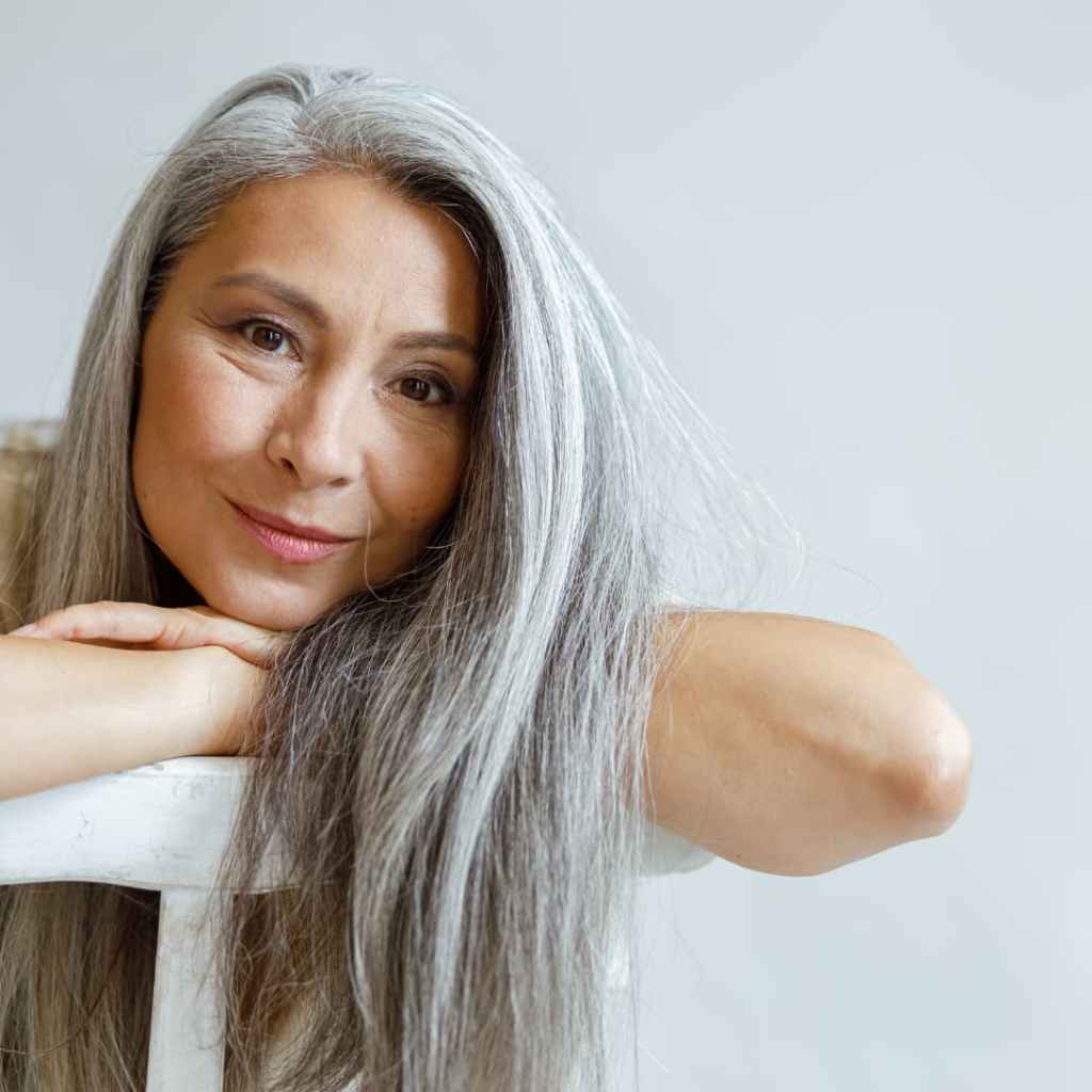 Portrait d’une femme aux longs cheveux gris, sourire doux et regard serein.