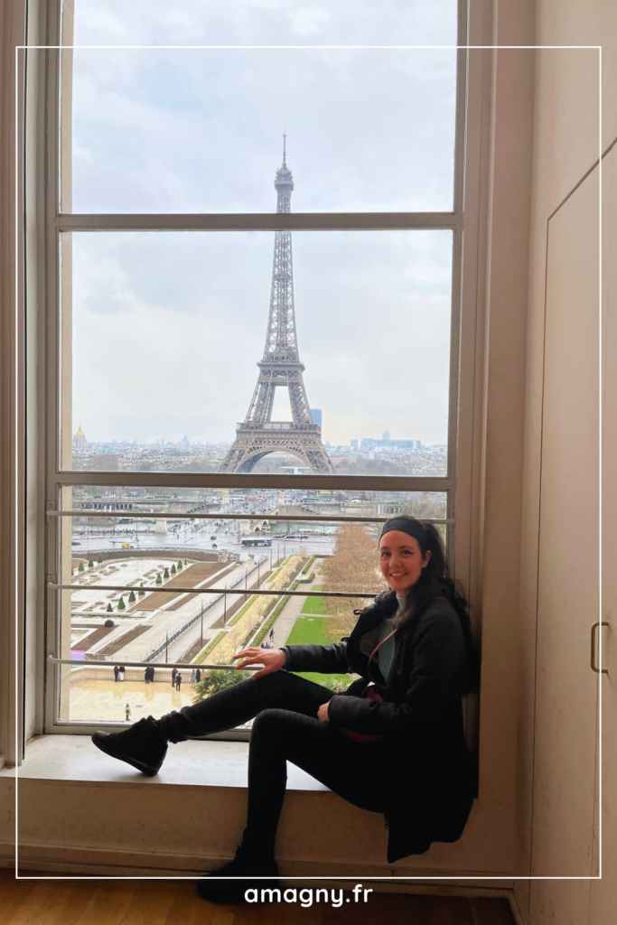 Personne assise prĂšs dâune fenĂȘtre avec vue sur la tour Eiffel.
