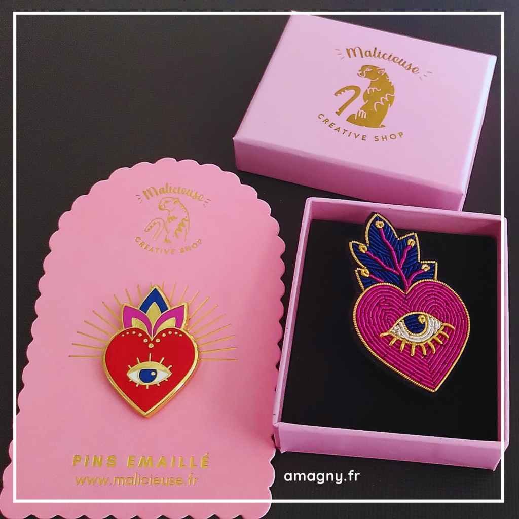 Broches Malicieuse en forme de cĆur avec Ćil, prĂ©sentĂ©es dans des boĂźtes roses.