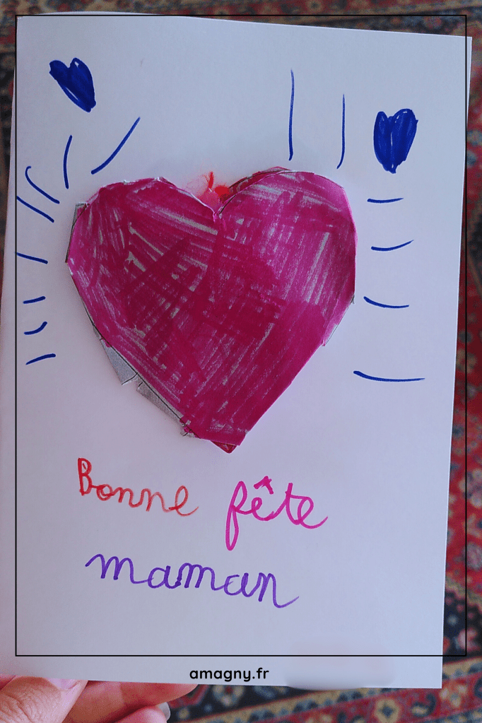 Carte faite maison avec un cĆur rose et lâinscription âBonne fĂȘte mamanâ rĂ©alisĂ©e par une enfant.