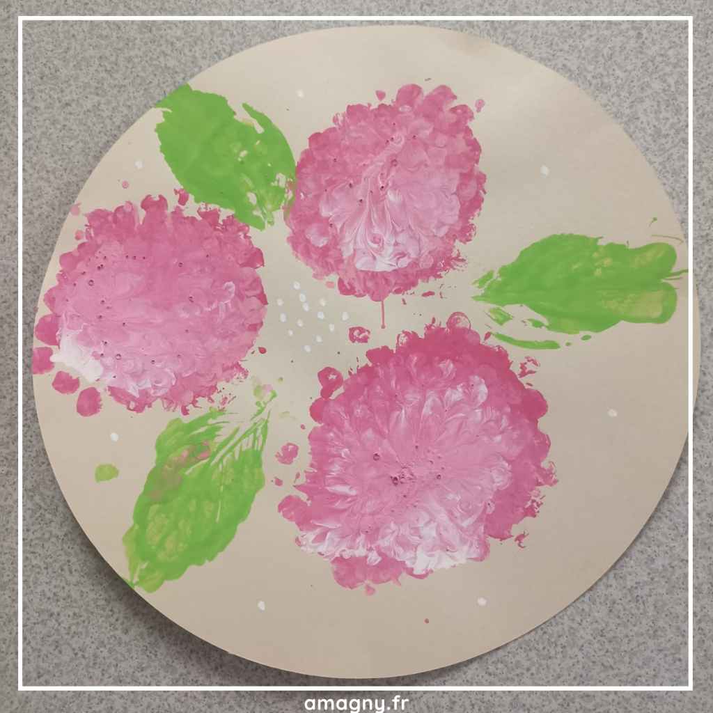 Rond en carton décoré par un enfant avec des hortensias roses et des feuilles vertes peints à l’éponge.