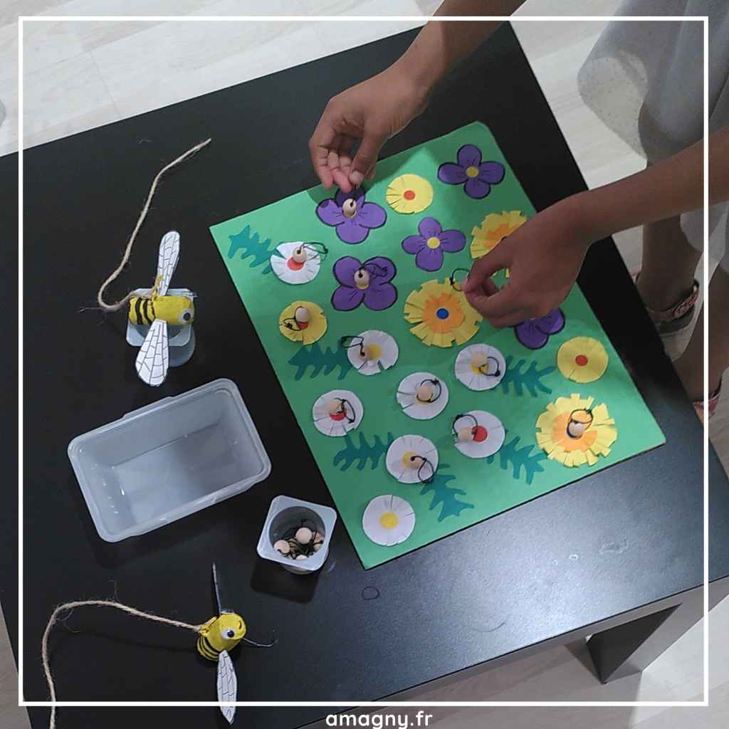 Enfant réalisant une activité manuelle de type Montessori avec des abeilles en feutrine sur des fleurs colorées pour apprendre la pollinisation.