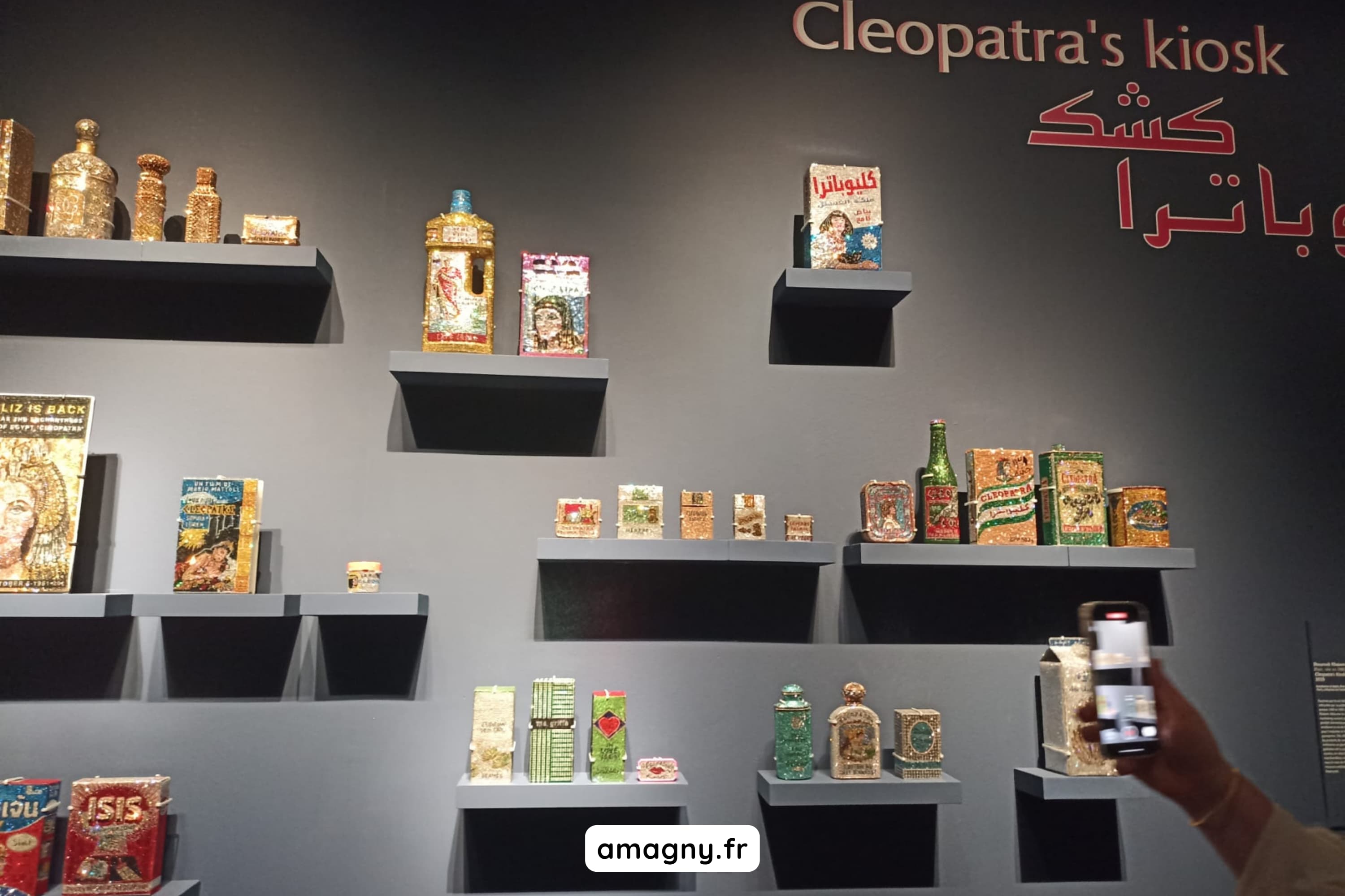 Installation “Cleopatra’s kiosk” présentant des objets décorés et colorés sur des étagères murales.