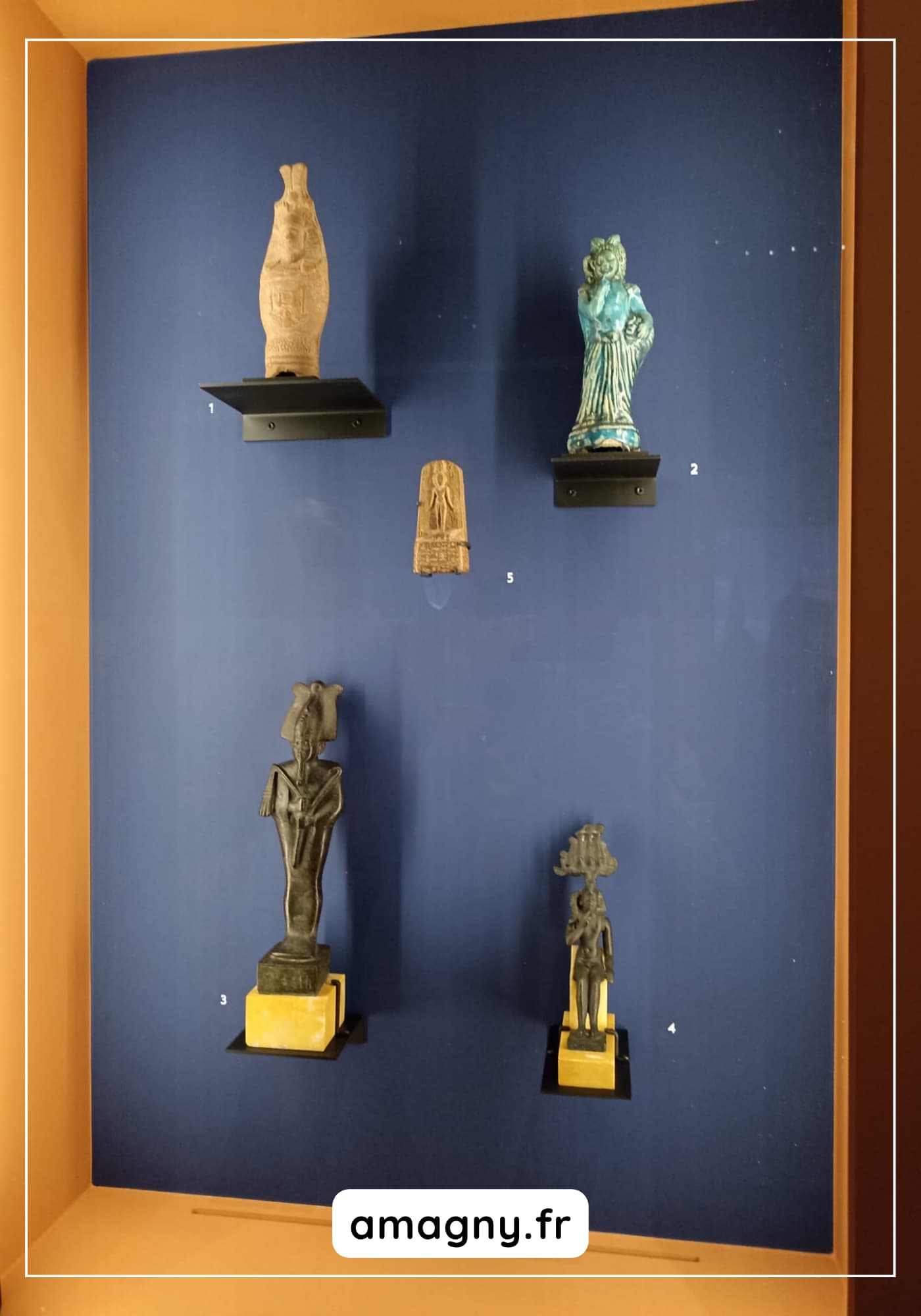 Figurines anciennes exposées en vitrine, comprenant statuettes humaines et animales sur fond bleu.