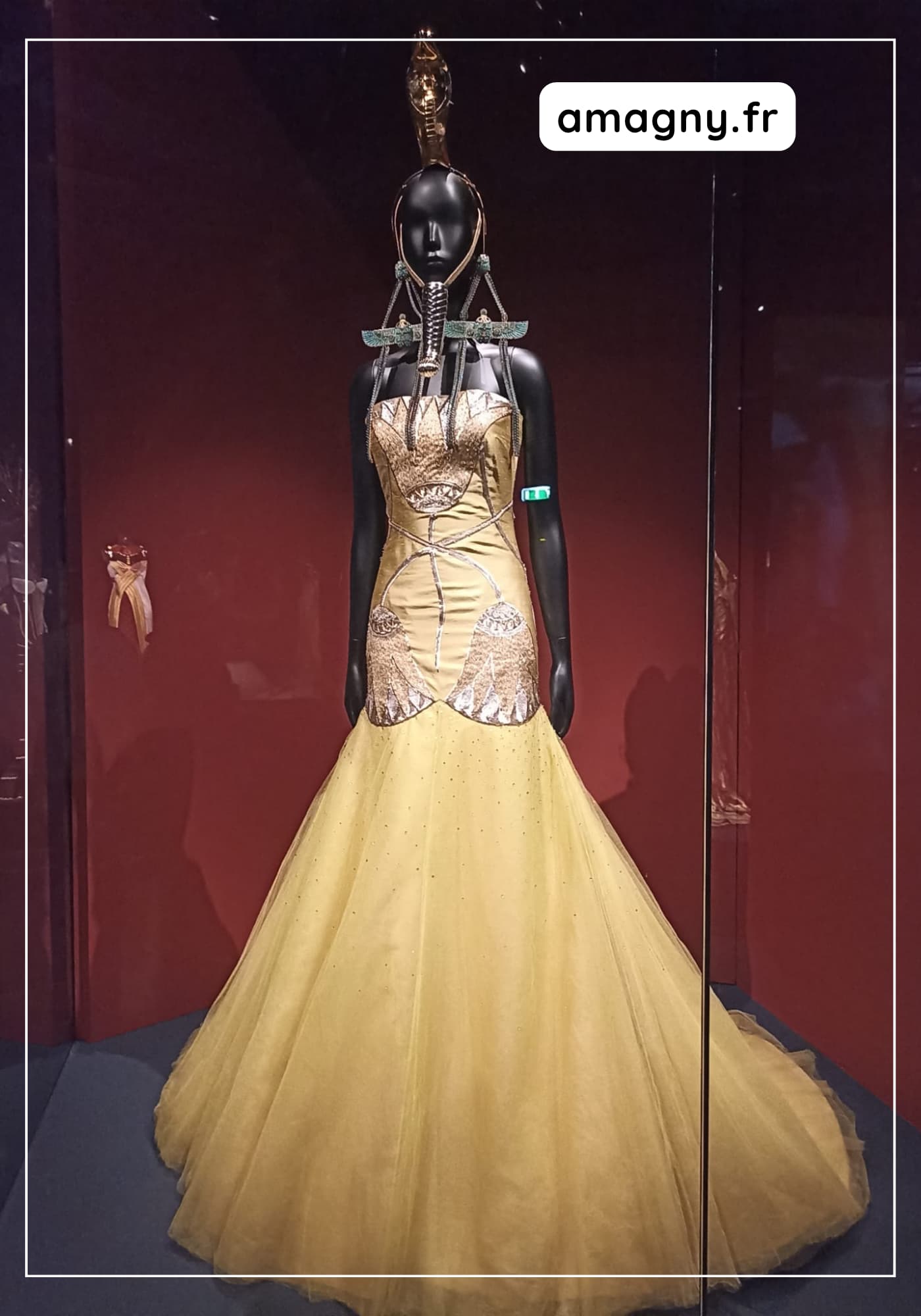 Mannequin portant une robe dorée d’inspiration égyptienne avec parure et coiffe cérémonielle.