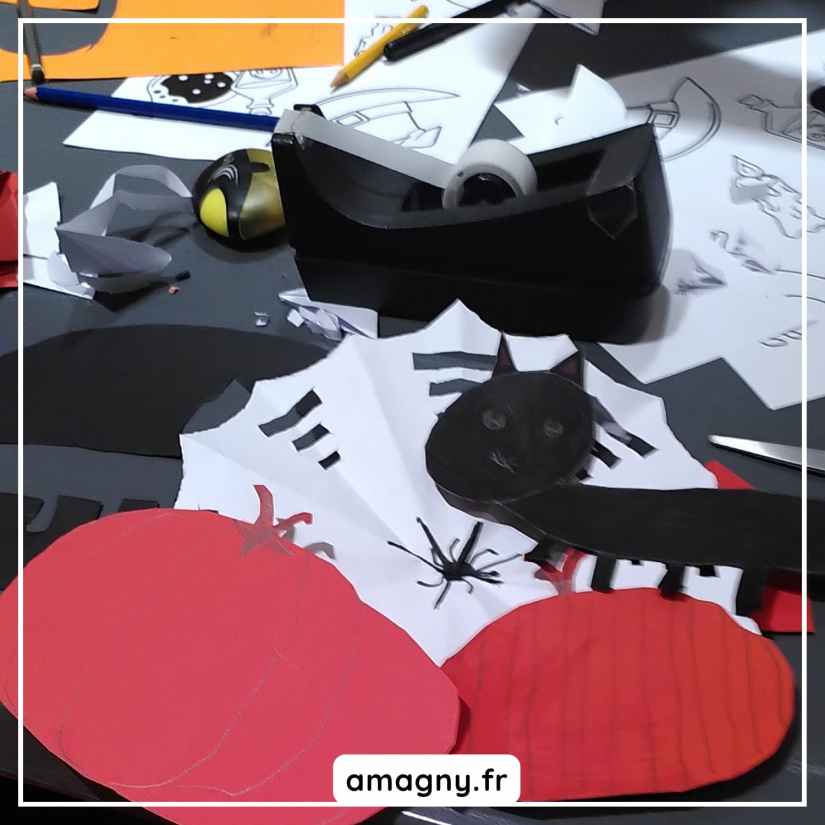 Photo d’un atelier créatif pour enfants sur le thème d’Halloween : découpes en papier de tomates, chats noirs et araignées, avec matériel de dessin et collage.