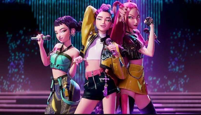 Trois personnages Mira, Zoey et Rumi animés sur scène dans le film Huntrix, en tenue futuriste, micro à la main, devant un décor lumineux bleu et violet.