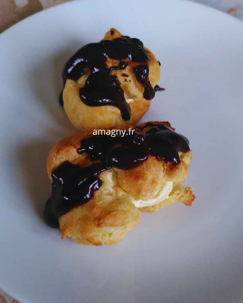 Profiteroles maison nappées de chocolat brillant, garnies de crème légère, sur une assiette blanche.