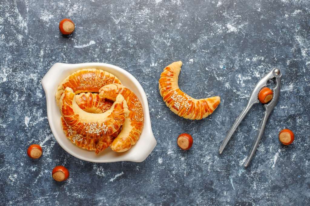 Croissants dorés aux noisettes, saupoudrés de graines de sésame sur assiette sombre.