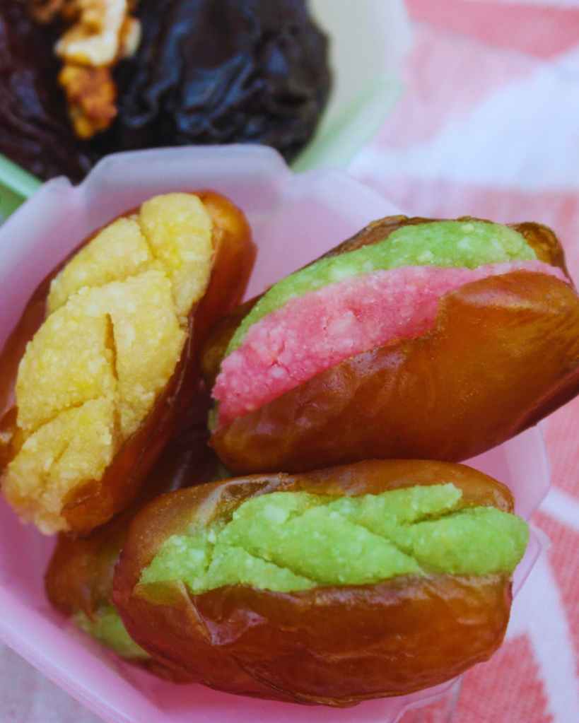 Dattes farcies de pâte d’amande colorée, présentées dans un écrin rose en ambiance festive.