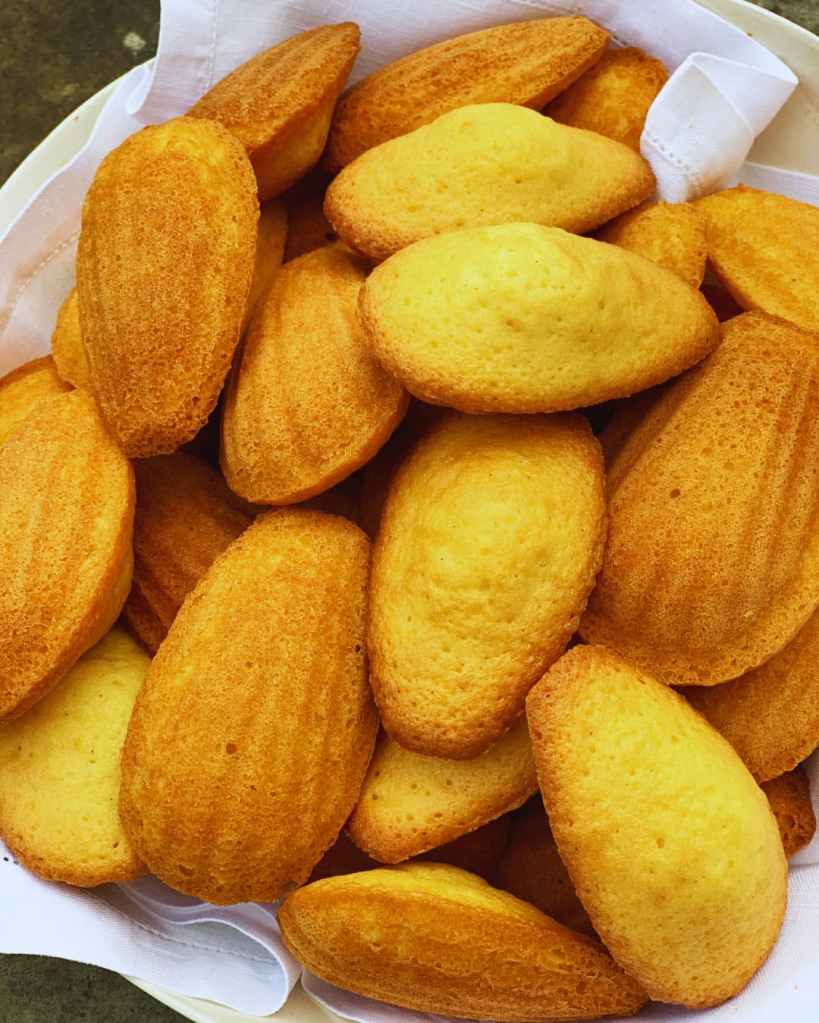 Madeleines dorées en forme de coquillage, présentées dans un panier avec un linge blanc.