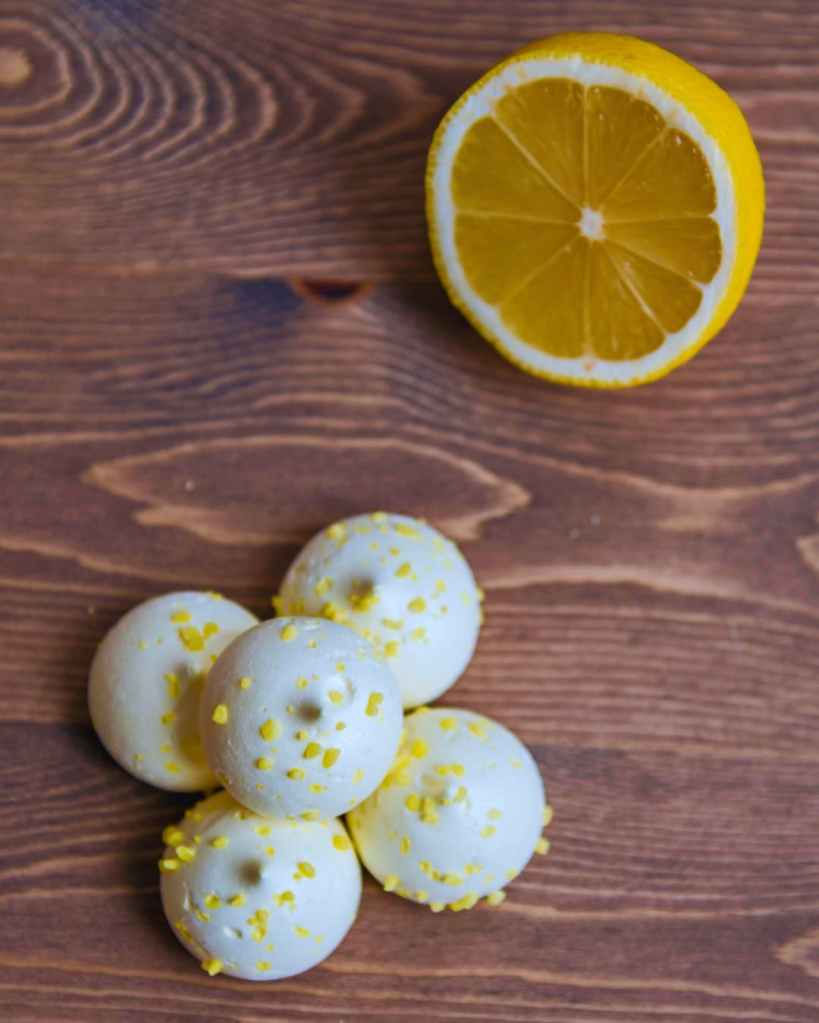 Meringues blanches décorées de zestes jaunes, posées sous un demi-citron sur fond bois.