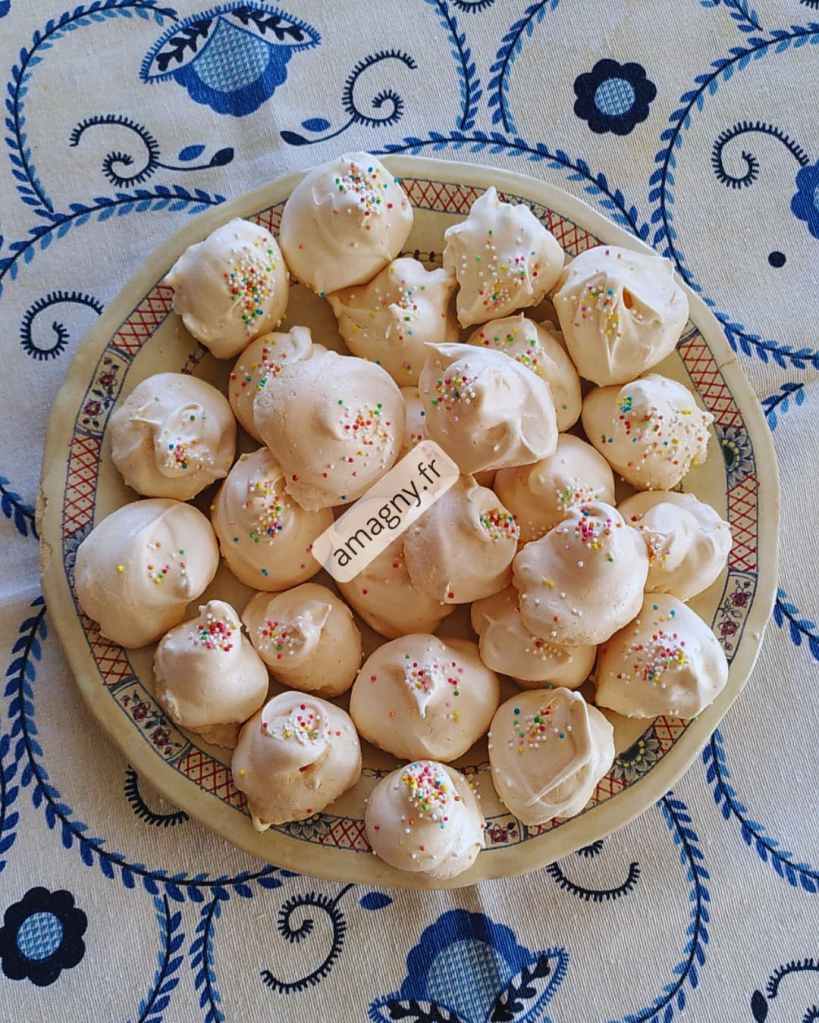 Assiette de meringues décorées de vermicelles colorés sur nappe à motif bleu. 