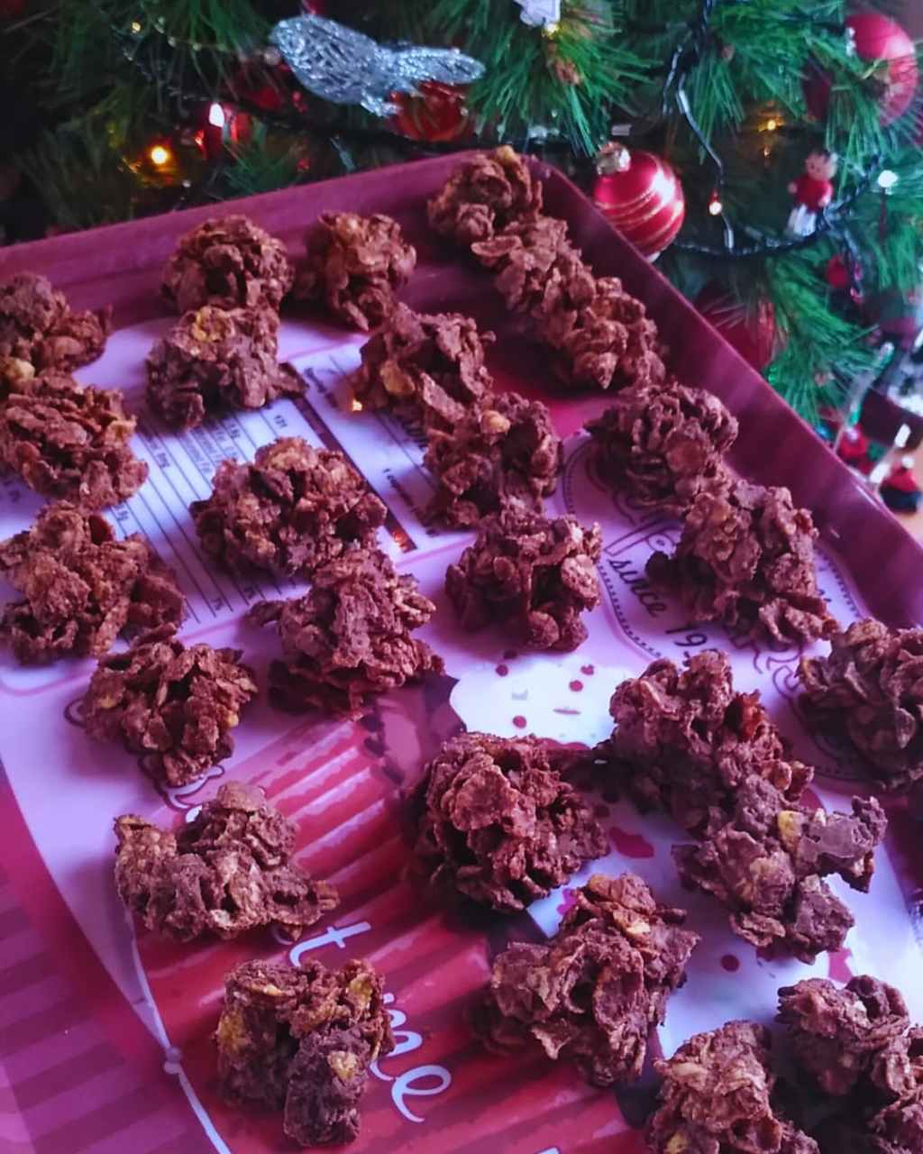 Plateau de roses des sables au chocolat, disposées devant un sapin décoré.