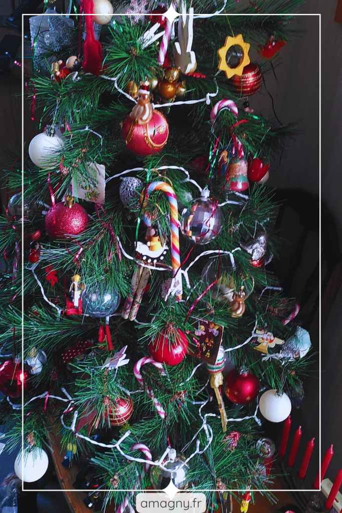 Sapin de Noël décoré avec boules colorées, figurines, guirlandes lumineuses et ornements originaux.