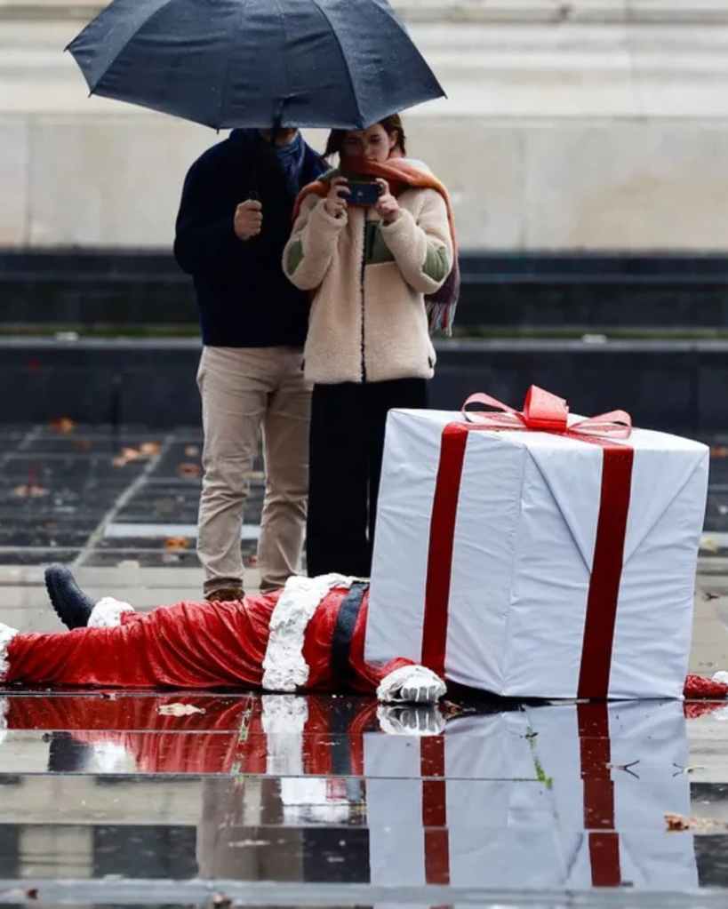 Sculpture urbaine de James Colomina représentant un Père Noël allongé avec un grand paquet cadeau sur la tête.