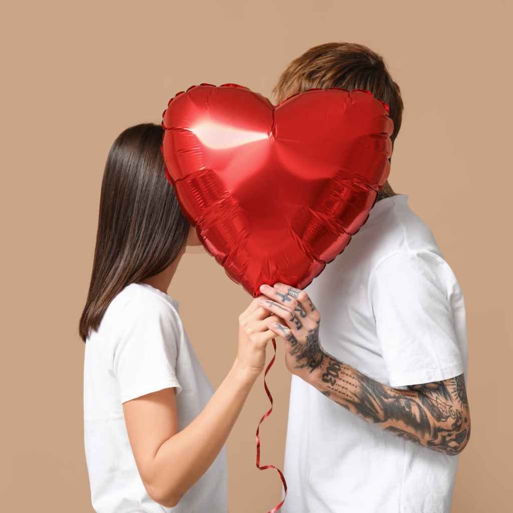 Couple tenant un ballon rouge en forme de cœur devant leurs visages, symbolisant amour et intimité dans un cadre minimaliste.